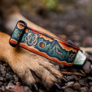 May include: A close-up of a dog collar with a colorful mountain and wolf design. The collar is made of durable nylon and features a black metal buckle.