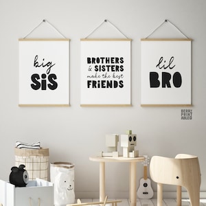 May include: Three black and white prints with the text "big sis", "brothers & sisters make the best friends", and "lil bro" hanging on a white wall in a child's room. The room has a wooden table and chair, a toy airplane, and a toy robot.