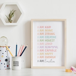 May include: A framed print with a white background and rainbow colored text that reads "I am kind, I am brave, I am strong, I am creative, I am honest, I am loved, I am beautiful, I am capable, I am happy, I am enough, I am Emilia".
