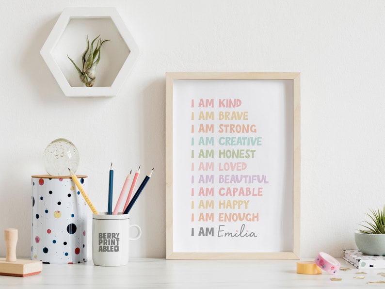 May include: A framed print with a white background and rainbow colored text that reads "I am kind, I am brave, I am strong, I am creative, I am honest, I am loved, I am beautiful, I am capable, I am happy, I am enough, I am Emilia".
