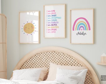 May include: Three framed prints with a rainbow, a sun, and a list of positive affirmations. The rainbow is pink, purple, blue, green, yellow, and orange. The sun is yellow with a smiling face. The affirmations are written in black text on a white background. The text reads "I am kind, I am brave, I am smart, I am unstoppable, I am strong, I am fearless, I am helpful, I am beautiful, I am unique, I am loved". The rainbow print has the name "Adalyn" written below it.