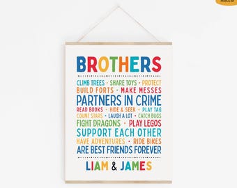 May include: A colorful art print with the word "BROTHERS" in large, rainbow-colored letters. The print lists fun activities like "CLIMB TREES" and "PLAY LEGOS", and is signed "LIAM & JAMES". The print is held by a wooden frame.