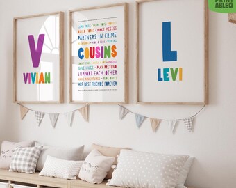 May include: Three framed art prints with wooden frames hang on a white wall. The prints feature the names "Vivian" and "Levi" in colorful letters, and a list of phrases about cousins. A garland of small flags hangs below.