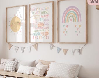 May include: Three framed art prints with a children's theme. One features a smiling sun, another has French text, and the third displays a rainbow with hearts. A garland of pennants hangs below the artwork, and pillows rest on a wooden storage unit.