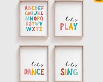 May include: Four framed art prints with a white background. One print displays the alphabet in colorful letters. The other three prints say "let's PLAY", "let's DANCE", and "let's SING" in colorful letters. The frames are light brown.