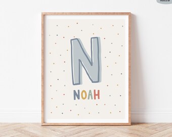 May include: A framed print featuring the letter "N" in light blue with a dark blue outline, above the name "NOAH" in colorful letters. The background is off-white with small, colorful polka dots. The print is in a wooden frame.