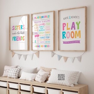 May include: Three framed prints with colorful text. The left print says "Sisters make the best friends". The middle print says "Playroom Rules" and lists rules like "Share", "Express your creativity", "Have Fun", and "Make Memories". The right print says "Katie & Kenzie's Play Room" with the text "Where the fun stuff happens" underneath.