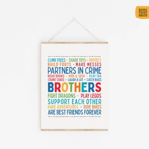 May include: A framed print with the words "Partners in Crime" and "Brothers" in colorful text. The print lists fun activities like climbing trees, building forts, and playing with Legos. The print is hung with a wooden bar and string.