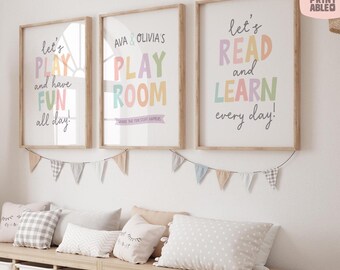 May include: Three framed prints with playful text in pastel colors: "Let's Play and have FUN all day!", "Ava & Olivia's PLAY ROOM", and "Let's READ and LEARN every day!". Below, a garland of pennants and a bench with pillows.