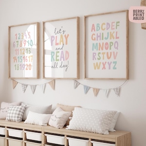 May include: Three framed prints with pastel-coloured numbers, letters, and a motivational quote. The prints are in wooden frames and are hanging above a bench with pillows and storage bins. A banner of small flags hangs below the prints.