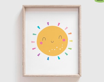 May include: A framed print featuring a cheerful, smiling sun with colorful rays. The sun is yellow with pink cheeks and a small, curved mouth. The rays are various colors, including pink, purple, blue, and orange. The print is in a light-colored wooden frame.