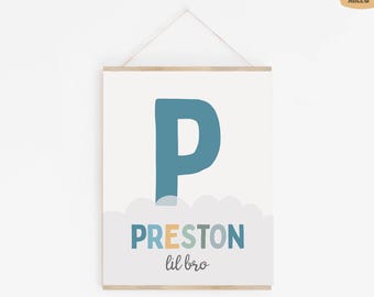 May include: A wall hanging print featuring a large blue letter P above the name PRESTON in multicolored block letters and the text lil bro in a dark gray script font. The design includes a light gray cloud graphic at the bottom.