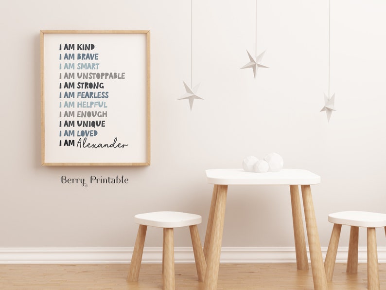 May include: A framed print with a white background and blue and gray text that reads "I am kind, I am brave, I am smart, I am unstoppable, I am strong, I am fearless, I am helpful, I am enough, I am unique, I am loved, I am Alexander". The print is hanging on a white wall with a small wooden table and two stools in front of it.