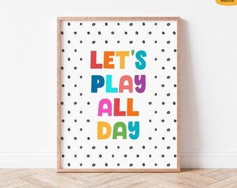 May include: A framed print with the words "LET'S PLAY ALL DAY" in colorful block letters. The background is white with scattered black polka dots. The frame is a light brown color.