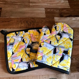 May include: A set of two black and yellow oven mitts with a lemon and pitcher design. The mitts are quilted and have a black trim.