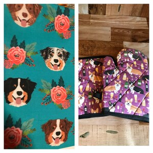 May include: Two kitchen items featuring a dog pattern. A teal blue tea towel with a repeating pattern of a floral design and a Bernese Mountain Dog. A purple oven mitt with a repeating pattern of a Corgi dog and wine glasses.