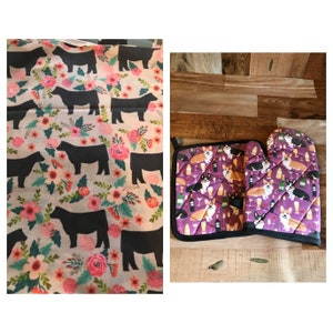 May include: A set of kitchen accessories featuring a pink and white tea towel with a black cow print and a purple pot holder and oven mitt with a corgi dog print.