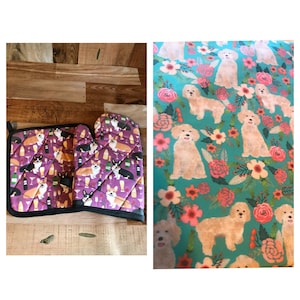 May include: A set of two purple oven mitts with a pattern of corgis and wine glasses. The mitts are on a wooden surface.