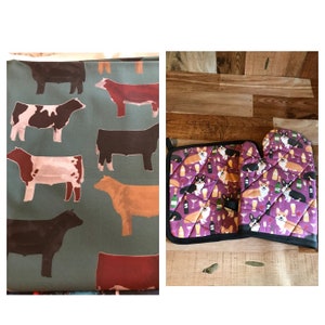 May include: A green fabric with a repeating pattern of brown, white, and red cows.  A purple pot holder and matching oven mitt with a repeating pattern of corgis drinking wine.