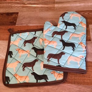 Könnte beinhalten: Ein Set aus zwei braunen, gesteppten Ofenhandschuhen mit blauem Hintergrund und einem Muster aus schwarzen und gelben Labrador Retrievern.