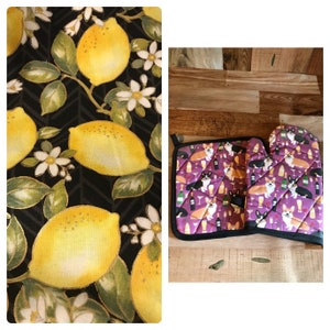 May include: Oven mitts and a pot holder with a purple pattern of corgi dogs, wine bottles, and glasses. The pot holder and oven mitts have black trim and are quilted. The left side shows a fabric with lemons and flowers.