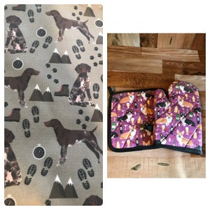 May include: A set of two purple oven mitts and a pot holder featuring a design of corgis enjoying wine and holding glasses. The background is a wooden surface.