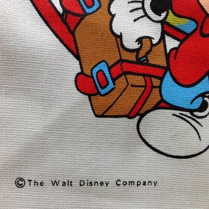 May include: A white canvas tote bag with a cartoon image of Mickey Mouse carrying a brown suitcase. The image is in red, blue, yellow, and black. The text "&copy; The Walt Disney Company" is printed in black at the bottom of the bag.