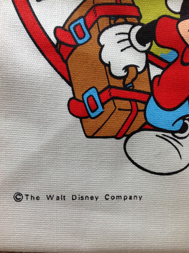 May include: A white canvas tote bag with a cartoon image of Mickey Mouse carrying a brown suitcase. The image is in red, blue, yellow, and black. The text "&copy; The Walt Disney Company" is printed in black at the bottom of the bag.