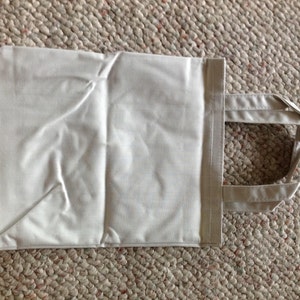 May include: A plain white tote bag with two handles. The bag is made of a soft, lightweight fabric.