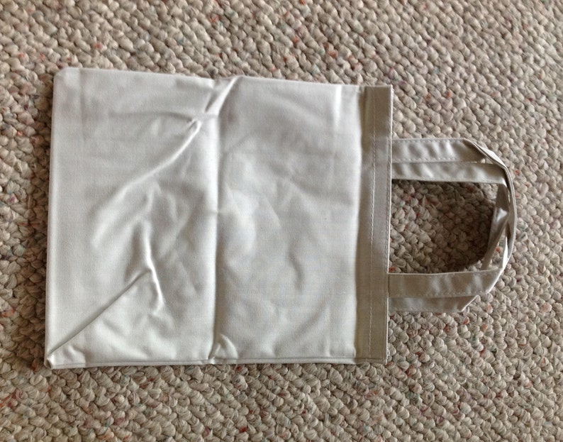 May include: A plain white tote bag with two handles. The bag is made of a soft, lightweight fabric.