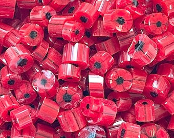 May include: A collection of small, cylindrical red glass beads, each featuring a distinct black floral pattern at the center. The beads have a glossy, translucent finish with visible vertical striations, creating a uniform appearance.