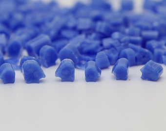 May include: Close-up of a pile of small, irregular, blue glass pieces. The pieces are scattered on a white surface, with some in focus and others blurred in the background. The glass has a translucent quality.