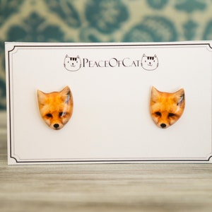 May include: A pair of fox face earrings on a white card with the text "Peace of Cat" printed on it.