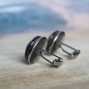 May include: A pair of silver cufflinks with a round, dark brown wood inlay. The cufflinks have a simple, elegant design.