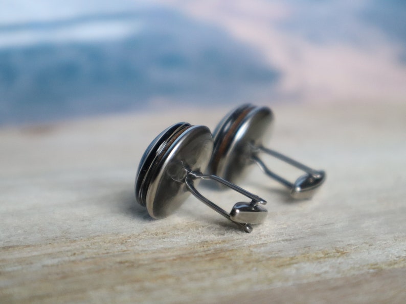 May include: A pair of silver cufflinks with a round, dark brown wood inlay. The cufflinks have a simple, elegant design.