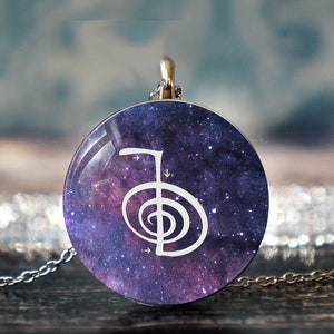 May include: A silver chain necklace with a round pendant featuring a white symbol on a purple and blue galaxy background.