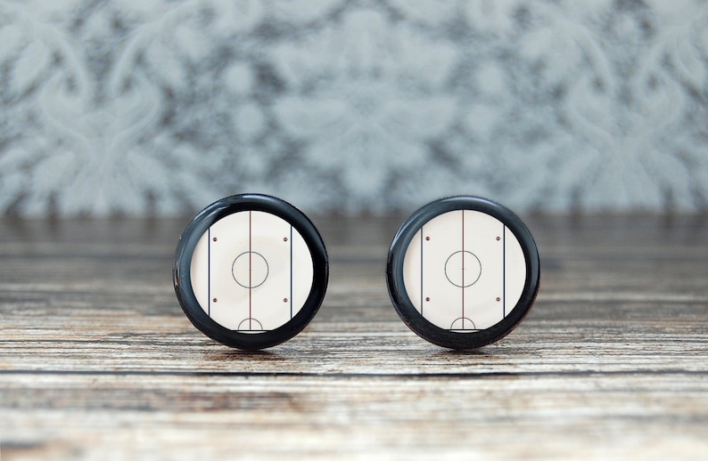 May include: A pair of black cufflinks with a white hockey rink design. The rink has a red center line and black lines for the face-off circles.