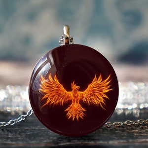 May include: A silver chain necklace with a round pendant featuring a fiery orange phoenix on a dark red background.