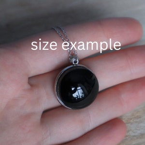 May include: A silver chain necklace with a black round pendant. The pendant is about 1 inch in diameter and has a silver bezel.
