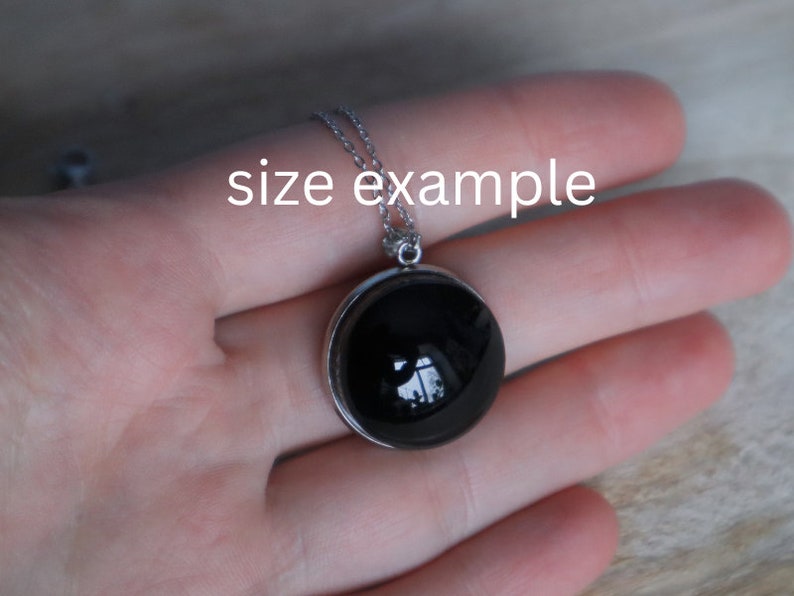 May include: A silver chain necklace with a black round pendant. The pendant is about 1 inch in diameter and has a silver bezel.