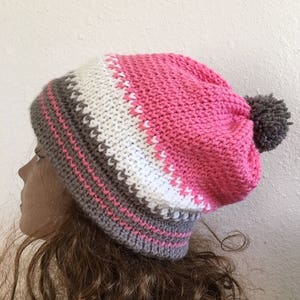 May include: A pink, white, and brown striped crocheted beanie with a brown pom pom on top.