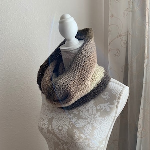 May include: A brown, beige, and cream knitted infinity scarf on a white mannequin.