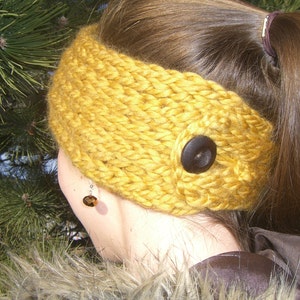May include: A yellow knitted headband with a brown button. The headband is worn by a person with long brown hair.
