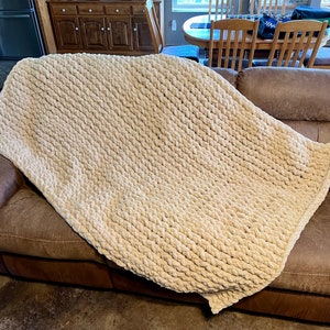 May include: A cream-colored chunky knit throw blanket draped over a brown leather couch.