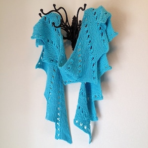 May include: A turquoise blue crocheted scarf with a lacy pattern hangs on a black metal hook. The scarf is draped in a way that shows off its intricate design.
