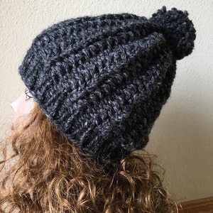 Op de afbeelding: Een grijze gebreide muts met een pluche pompon bovenop.
