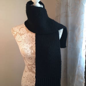 May include: A black knit scarf with a soft, fuzzy texture. The scarf is draped over a white mannequin.