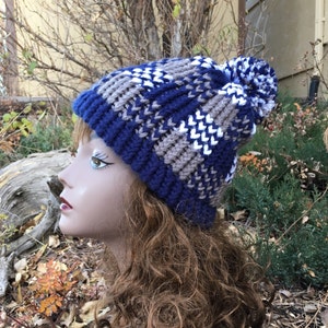 May include: A blue, brown and white knitted beanie with a pom-pom on top.