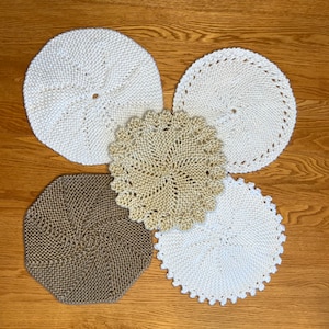 May include: Five crocheted coasters in different patterns and colors. Two are white, one is beige, and two are brown.