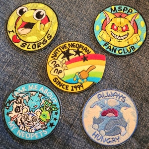 May include: Five embroidered patches featuring Neopets characters. The patches are circular and feature various colors, including yellow, blue, green, and red. The patches feature text such as "I Slorg", "MSPP Fan Club", "Native Neopian Since 1999", "Ask Me About My Neopets", and "Always Hungry".